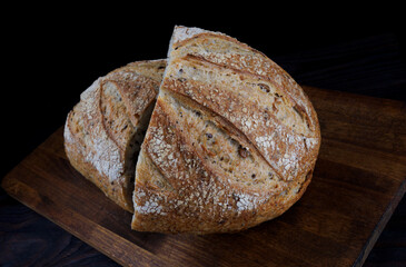 A loaf of designer bread cut in half with seeds on a wooden board. Art bread.