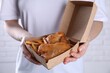 Woman holding fish and chips in paper box near white brick wall, closeup