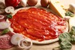 Pizza base smeared with tomato sauce and products on parchment, closeup