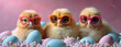 Three adorable chicks wearing colorful glasses sitting among pastel-colored eggs on a soft pink background, conveying a whimsical and cute Easter theme.