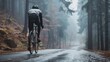 A cyclist in a gray jacket and black pants riding a bicycle on a wet foggy road through a forest.