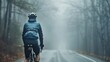 A lone cyclist in a blue jacket and helmet riding a bicycle on a foggy tree-lined road.