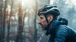 © iuricazac - A man with a beard wearing a black helmet and a blue jacket riding a bicycle through a misty forest.