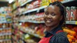 A smiling woman in a red apron standing in a grocery store aisle filled with various packaged goods.