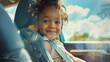 A joyful young child with curly hair wearing a seatbelt sitting in a car seat looking out of a car window at a sunny day with clouds.