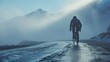 A lone cyclist pedaling through a misty mountain pass with a dramatic sky and snow-capped peaks in the background.