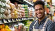 © iuricazac - A smiling man in a blue shirt and apron standing in a well-stocked grocery store aisle with various packaged goods and fresh produce.