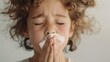 Young child with curly hair closed eyes and a tissue held to the nose suggesting a moment of comfort or distress.