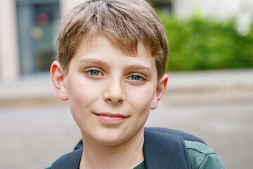 Happy preteen kid boy with backpack or satchel. Schoolkid in on the way to elementary or middle school on warm sunny summer day. Healthy child outdoors on the street in the city .