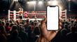A hand holding a phone displaying a empty blank white screen in front of a crowded boxing ring with two boxers