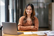 © Wasana - A focused young woman working intently at desk with a laptop and notebook in a bright, modern office setting.