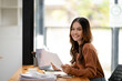 © Wasana - A focused businesswoman reviews documents at her desk with laptop and coffee