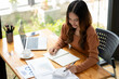 © Wasana - A focused young woman working intently at desk with a laptop and notebook in a bright, modern office setting.