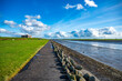 Waterfront of Husum with meadow on the left and sea on the right, beautiful clouds and wind turbines in the background, wide angle shot, Germany