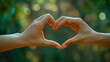 A pair of hands create a heart symbol against a blurry green background, invoking themes of love and peace