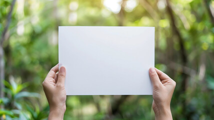 Wall Mural - hands holding white blank paper sheet on blur nature background.