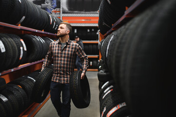 Wall Mural - Glad male customer taking new tires in the supermarket for buying. He looks happy. Big shopping mall with car goods