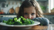 Photo capturing the moment of reluctance as a child stares at a plate of green leafy vegetables their expression a mix of dismay and stubborn refusal