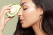 Girl with beautiful profile and shiny hair presses half of fresh avocado to back of her nose.