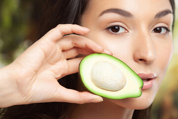 Wall Mural - Young beautiful woman holding avocado half in her hands on forest background