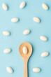 White soft gelatin capsules with wooden spoon on light blue background. Concept of probiotic supplement, vitamins and painkiller addiction.