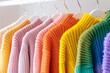 A row of brightly colored sweaters hanging on a rack. The colors are pink, orange, yellow, green, and purple. Concept of warmth and cheerfulness