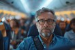 A middle-aged man with glasses sits on a plane looking pensively towards the camera