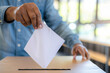 Close-up black male hand putting voting card into the ballot box. Vote on free democratic elections or referendum.