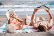 Two young women lying on the sand on the beach enjoying themselves while reading. relax