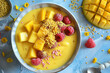 A bowl of fruit with raspberries and mangoes. The bowl is white and has a yellowish tint