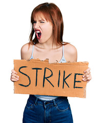 Wall Mural - Redhead young woman holding strike banner cardboard angry and mad screaming frustrated and furious, shouting with anger. rage and aggressive concept.