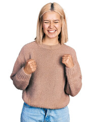 Poster - Beautiful young blonde woman wearing brown sweater excited for success with arms raised and eyes closed celebrating victory smiling. winner concept.