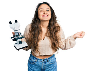 Sticker - Young hispanic girl holding microscope screaming proud, celebrating victory and success very excited with raised arm