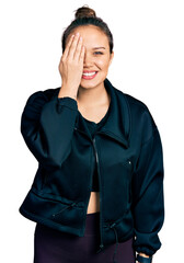 Sticker - Young hispanic girl wearing sportswear covering one eye with hand, confident smile on face and surprise emotion.