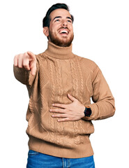 Wall Mural - Young hispanic man wearing casual clothes laughing at you, pointing finger to the camera with hand over body, shame expression