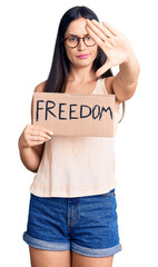 Canvas Print - Young beautiful caucasian woman holding freedom banner with open hand doing stop sign with serious and confident expression, defense gesture