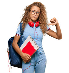 Poster - Beautiful caucasian teenager girl holding student backpack and books with angry face, negative sign showing dislike with thumbs down, rejection concept