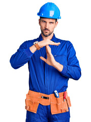 Canvas Print - Young handsome man wearing worker uniform and hardhat showing middle finger, impolite and rude fuck off expression