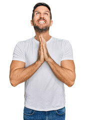 Canvas Print - Handsome man with beard wearing casual white t shirt begging and praying with hands together with hope expression on face very emotional and worried. begging.