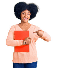 Wall Mural - Young african american girl holding book smiling happy pointing with hand and finger