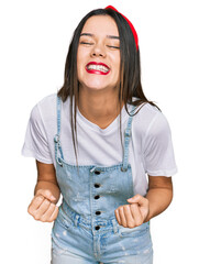 Wall Mural - Young hispanic girl wearing casual clothes very happy and excited doing winner gesture with arms raised, smiling and screaming for success. celebration concept.