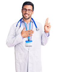 Canvas Print - Young hispanic man wearing doctor uniform and stethoscope smiling swearing with hand on chest and fingers up, making a loyalty promise oath