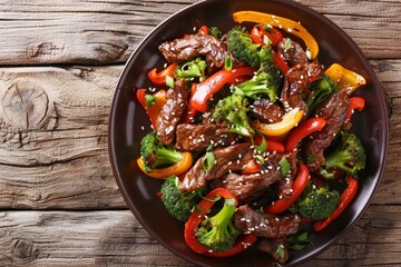Wall Mural - Close up view of teriyaki beef with colorful bell peppers broccoli and sesame seeds on a table