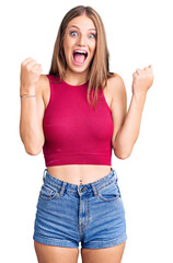 Young beautiful blonde woman wearing elegant summer shirt celebrating surprised and amazed for success with arms raised and open eyes. winner concept.