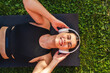 Top view of one young girl holding her wireless headphones while laying on her yoga mat on the grass taking rest after training