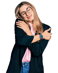 Wall Mural - Hispanic young woman wearing business jacket and glasses hugging oneself happy and positive, smiling confident. self love and self care