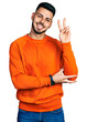 © Krakenimages.com - Young hispanic man with beard wearing casual orange sweater smiling with happy face winking at the camera doing victory sign. number two.