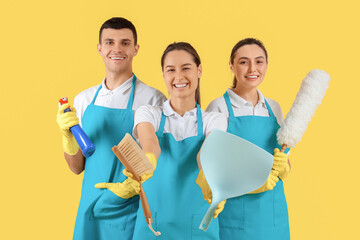 Canvas Print - Workers of cleaning service with supplies on yellow background