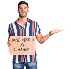 Wall Mural - Young handsome hispanic man holding we need a change banner celebrating victory with happy smile and winner expression with raised hands