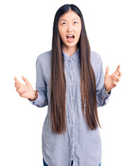 Sticker - Young beautiful chinese woman wearing casual shirt crazy and mad shouting and yelling with aggressive expression and arms raised. frustration concept.